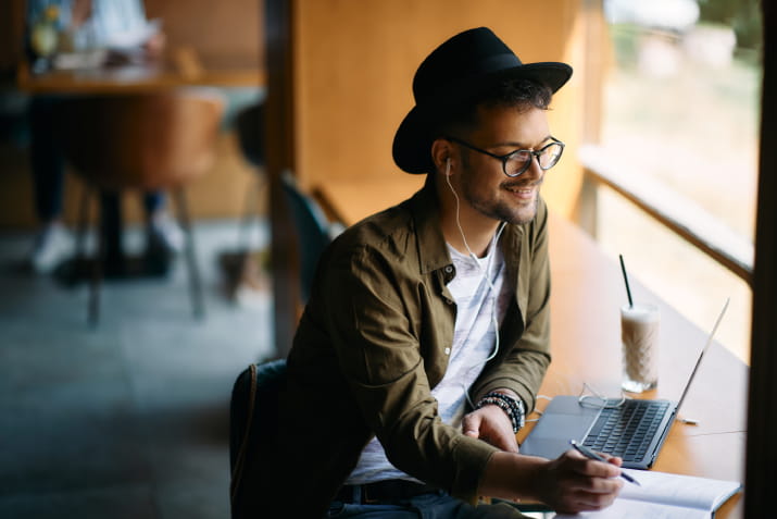 A young man sitting in a cafe and smiling at a laptop 